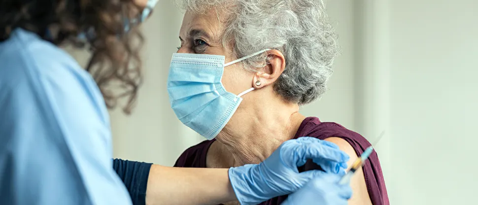 A senior woman is receiving a vaccine to her upper arm from a healthcare professional.