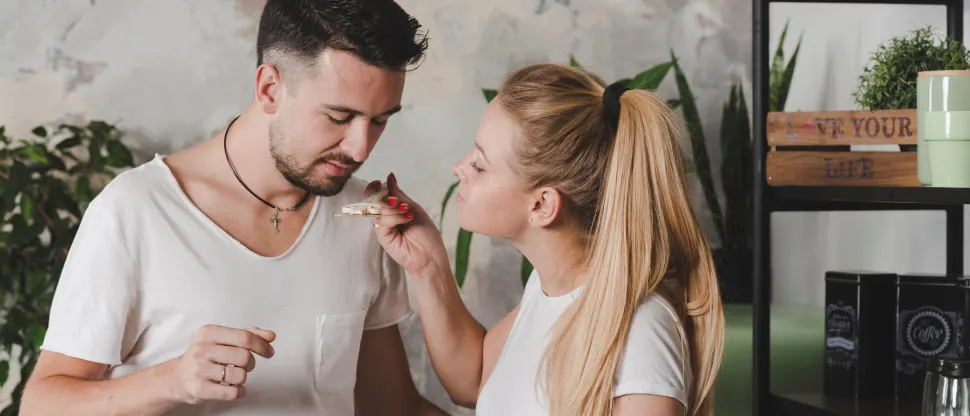 Fiatal pár áll a konyhában. A nő egy fakanalat tart a férfi elé, hogy megkóstolja a főztjét