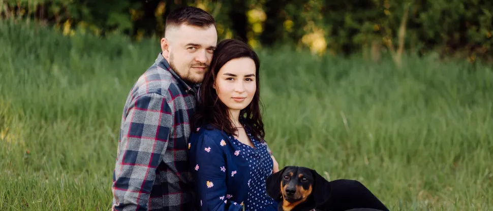 Mosolygó fiatal pár ül a fűben a kiskutyájával