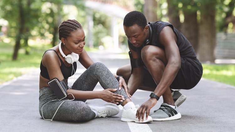 Biegacz podchodzący do drugiego biegacza który doznał kontuzji kostki