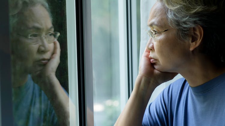 Smutna samotna starsza kobieta patrzy przez okno