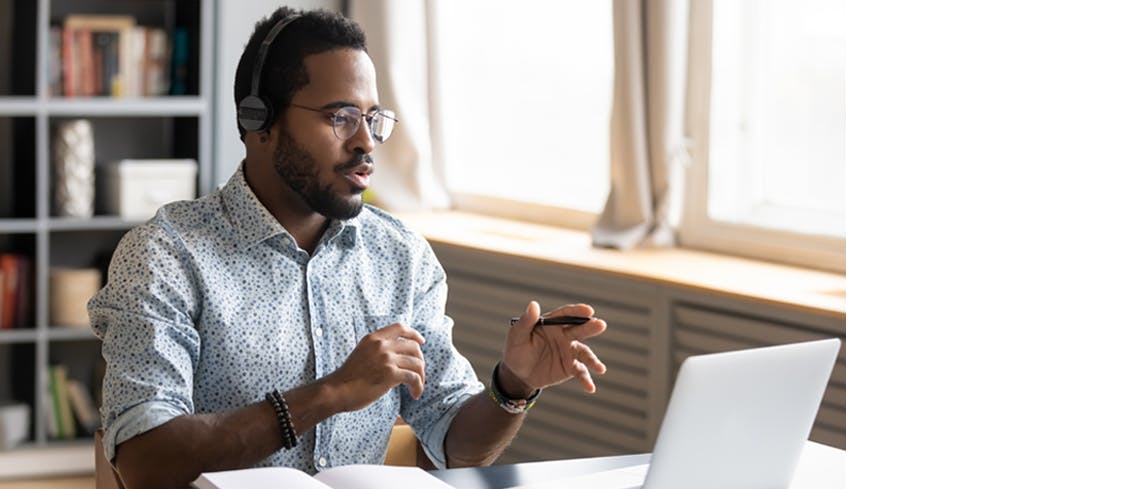 Um homem usando fones de ouvido fazendo uma chamada online no laptop.