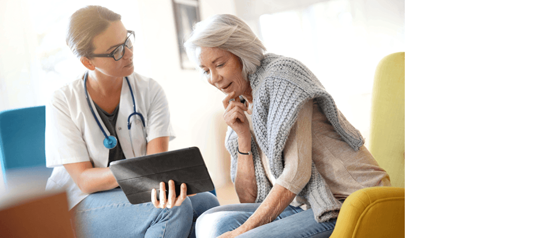 Uma médica com um estetoscópio ao redor do pescoço mostrando algo para uma senhora mais velha em um tablet.