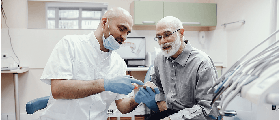 Um dentista e um paciente olham para uma boca modelo e dentes juntos