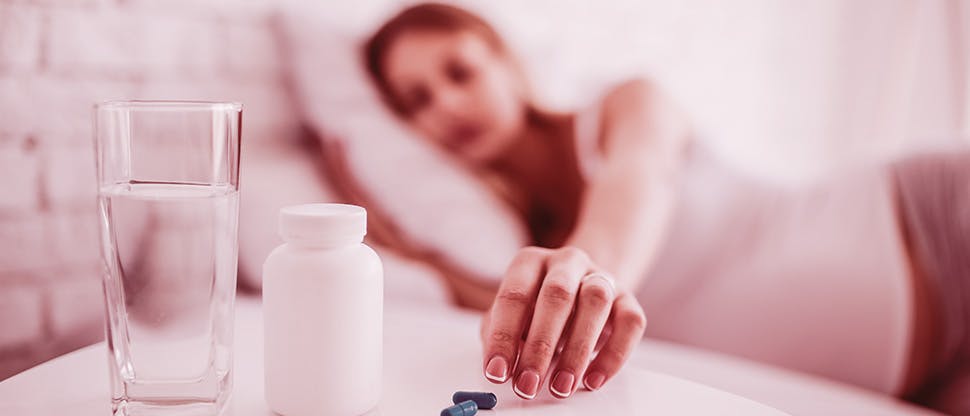 crop-ill-woman-taking-pills-in-bed