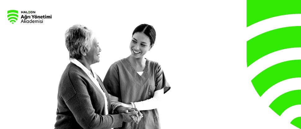 Genç bir sağlık uzmanı yaşlı bir kadın hastanın kolunu tutarak onunla gülümseyerek konuşuyor