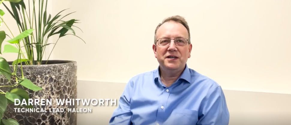 Darren Whitworth Haleon bilim insanının görüntüsü, gözlük takıyor ve mavi bir gömlek giyiyor, büyük bir saksı bitkisinin yanında oturuyor.
