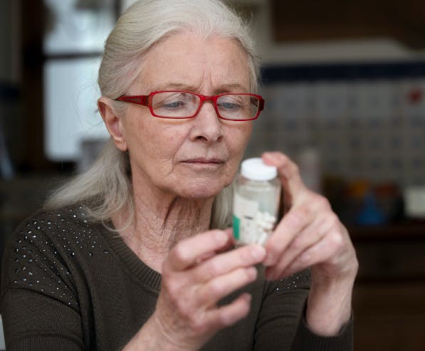 Een oudere vrouw met bril leest de verpakking van een medicijn