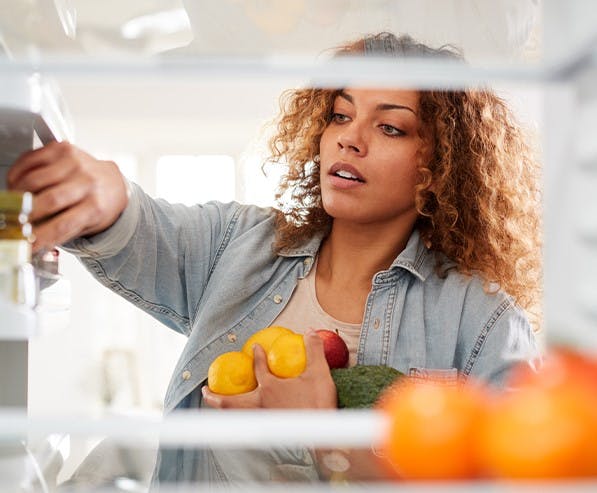 Een vrouw staat voor een open koelkast met fruit in haar handen