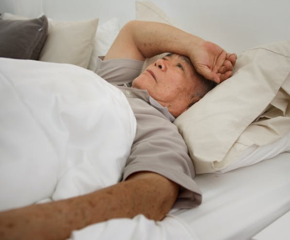 Een oudere man ligt in bed en vertoond kenmerken van ziekte