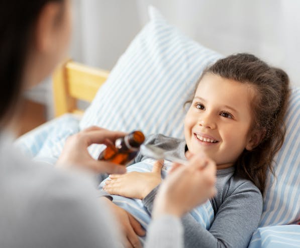 Vrouw giet medicijnen in een lepel terwijl een kind in bed naar haar lacht