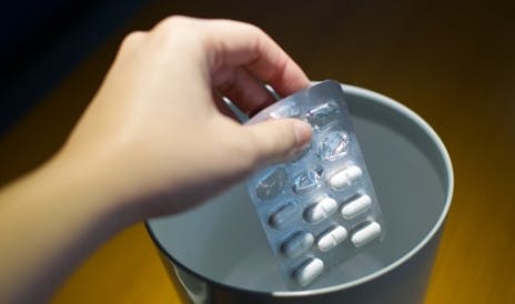 Person discarding a pill packaging into a metal bin