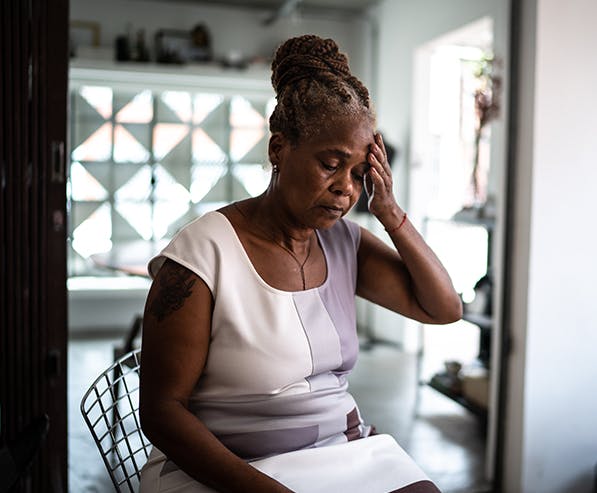 Senior woman sitting and holding her hand on her forehead showing signs of pain