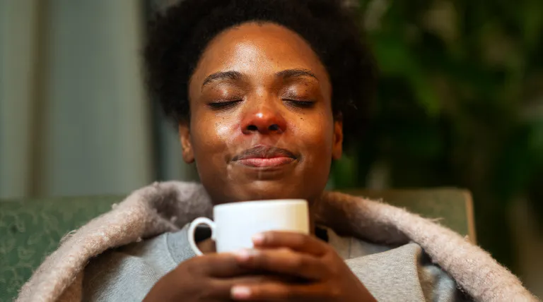 Femme qui tient une grosse tasse, à l’intérieur, qui profite du soulagement apaisant de la vapeur qui s’échappe de la tasse.