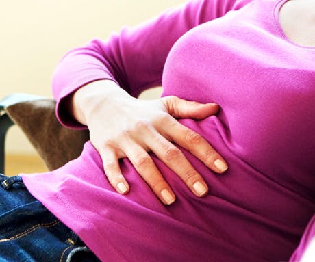 A woman in pink with hands on her stomach.