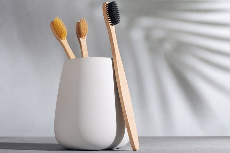White cup with two wooden toothbrushes in the cup and another toothbrush standing in front of it