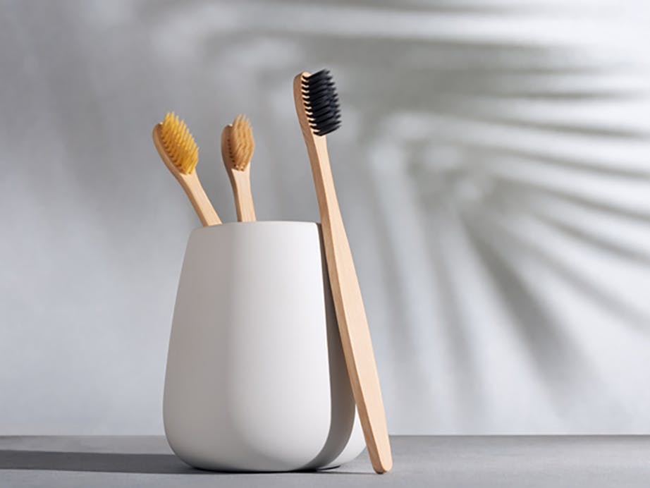 White cup with two wooden toothbrushes in the cup and another toothbrush standing in front of it