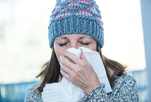 Mature woman with a cold and symptoms of congestion and blocked nose blows her nose into a tissue.