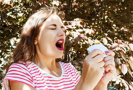 Eine junge Frau ist gerade kurz vorm Nießen wegen Heuschnupfen, eine Allergie die durch Otri-Allergie Nasenspray gelindert werden kann