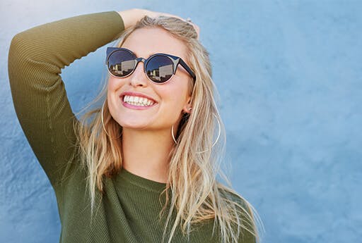 Eine stylishe junge Frau lächelt, weil sie Symptome von Heuschnupfen verhindert hat, indem sie zuhause blieb und Nasensprays benutzte.