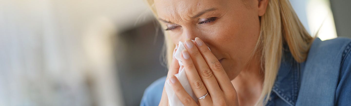 Ältere Frau mit Erkältungssymptomen schnäuzt in ein Taschentuch.