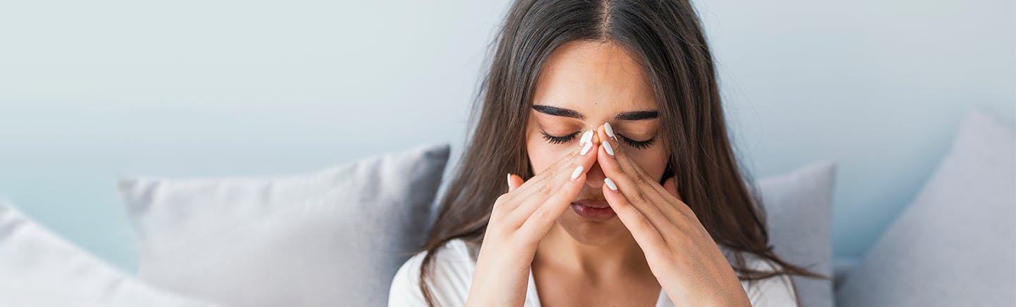 Frau reibt sich die Nase, was ein Symptom einer Nasennebenhöhlenentzündung sein könnte.