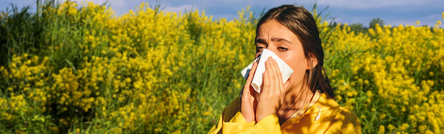 Frau niest aufgrund von Heuschnupfen, der durch Einatmen von Pollen hervorgerufen werden kann.