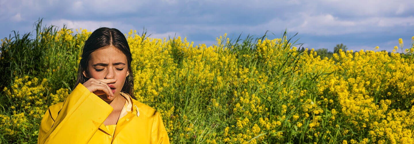 Young girl surrended by blooming flowers in park sneezes due to hay fever.