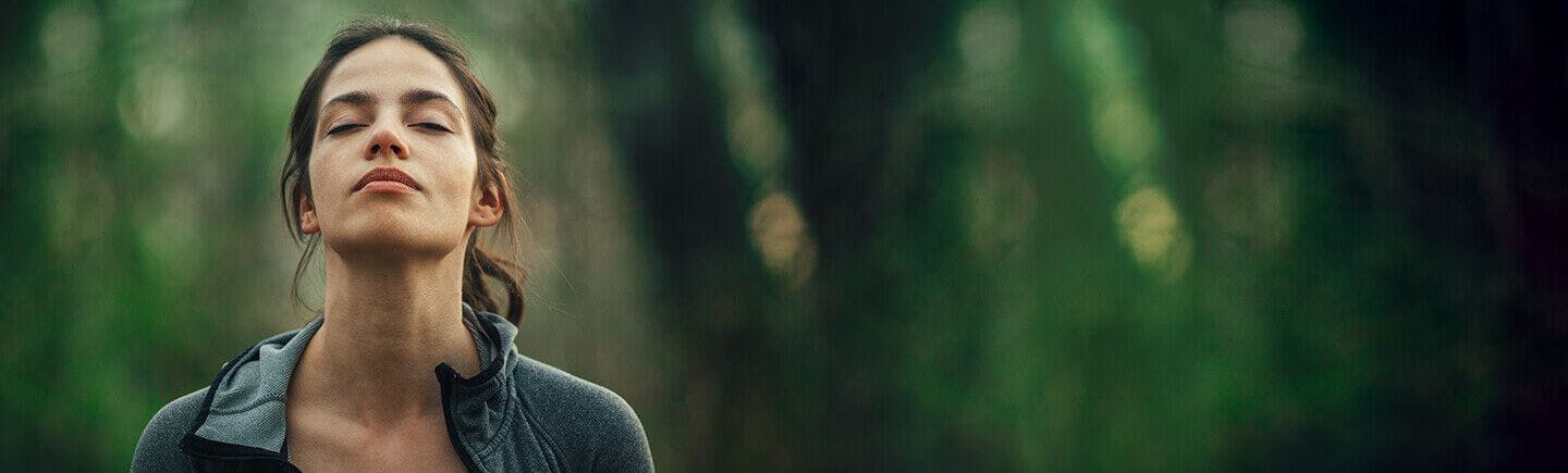 A young woman appears to be breathing with her unblocked nose in a forest