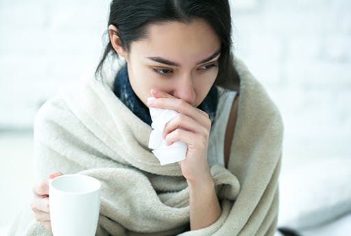 A young woman appears to drink a hot beverage to get relief from the cold and decongest her nose