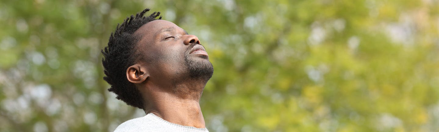 Young man in the middle of a forest breathes fresh air, as he is not exposed to air pollution.