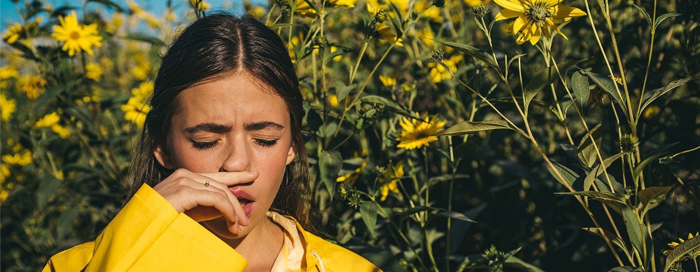 Young girl surrended by blooming flowers in park sneezes due to hay fever.