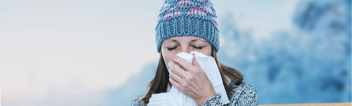 Mature woman with a cold and symptoms of congestion and blocked nose blows her nose into a tissue.
