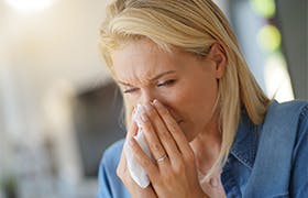 Vrouw van middelbare leeftijd met allergie die haar neus snuit