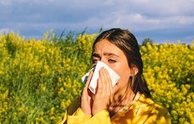 Vrouw niest door hooikoortsallergie, die veroorzaakt kan zijn door het inademen van stuifmeel.