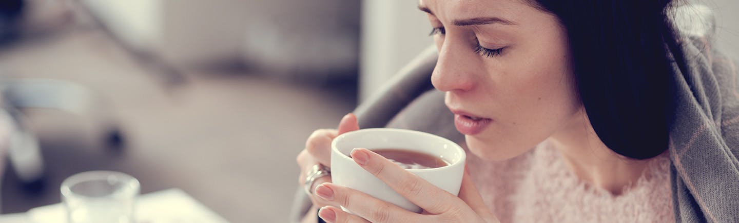 Une femme boit une bonne tasse de thé après avoir utilisé son spray nasal Otrivine.