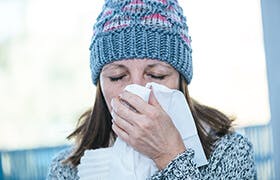 Une femme d'âge mûr enrhumée avec des symptômes de congestion et de nez bouché se mouche dans un mouchoir en papier.