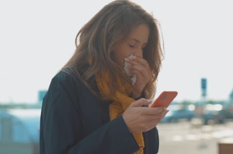  Ragazza che guarda il telefono e si soffia il naso per il raffreddore - Rinazina 