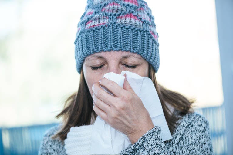 Donna con cappello invernale che si soffia il naso - Rinazina