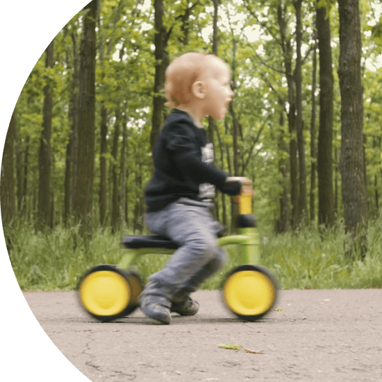 Toddler riding a tricycle through a forest 