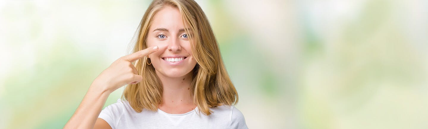 Dame med lyst hår og hvit t-skjorte peker mot nesen og er fornøyd med å ha gjenopprettet nesens normale funksjon med Otrivin  