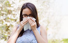 Kvinne med mørkt hår står ute og snyter seg i et papirlommetørkle på grunn av allergi  