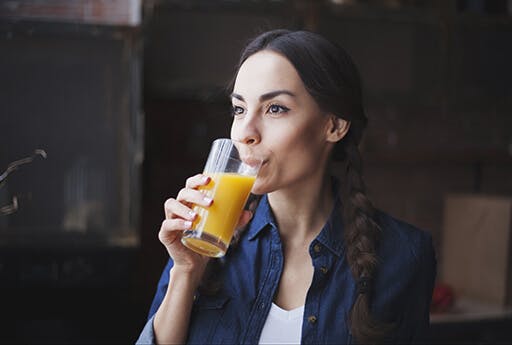 Молодая женщина пьет апельсиновый сок, полный витамина С, чтобы поддерживать гидратацию своего организма, если она страдает от сенной лихорадки.