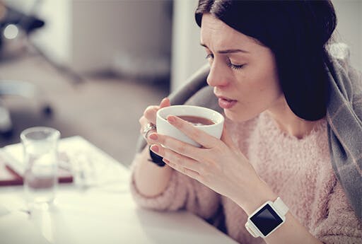 Woman drinks a cup of tea in order to stay hydrated and to prevent cold symptoms such as sore throat, cough and runny nose.