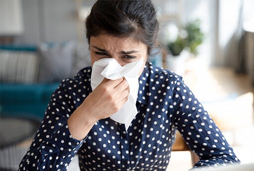 Young woman sneezes into tissue as she tries to relieve її congested nose.