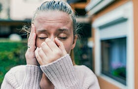 Молодая женщина страдает от последствий загрязнения воздуха, которые включают раздражение дыхательных путей, заложенность носа, обострение респираторных заболеваний и раздражение глаз.
