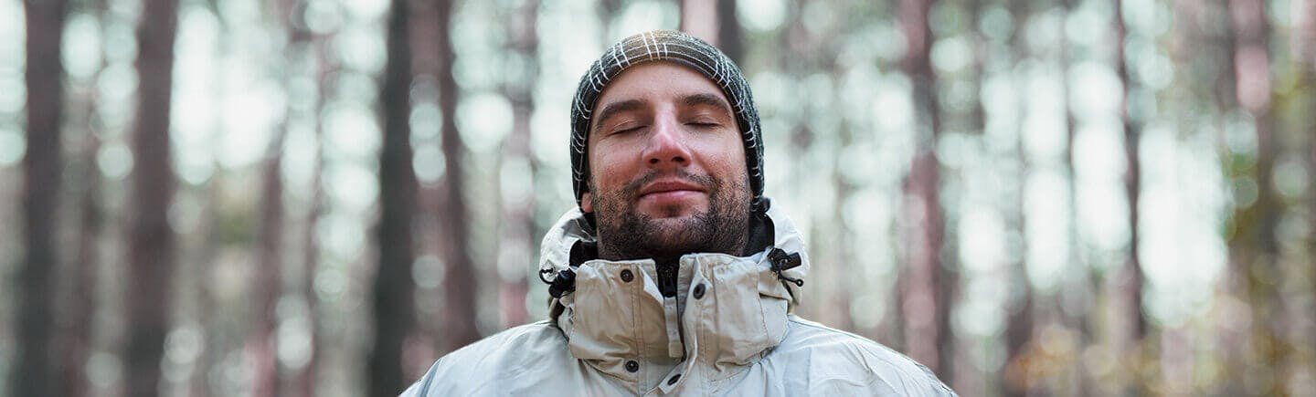 Young man in the middle of a forest breathes fresh air, as he is not exposed to air pollution.