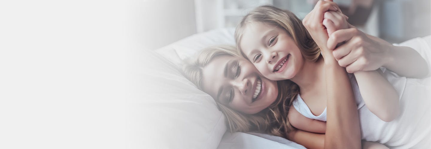 Mother and daughter embracing and smiling as they lay in bed together