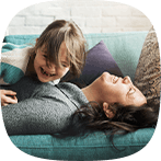 Giggling young girl lies on top of her mother on the sofa