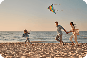 Young couple running along the sand at the beach with their young daughter